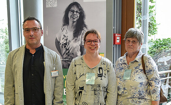 Drei Menschen stehen vor einem Ausstellungsbanner