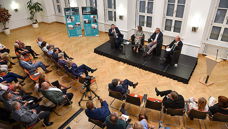 Menschen sitzen im Halbrund und blicken auf Podium