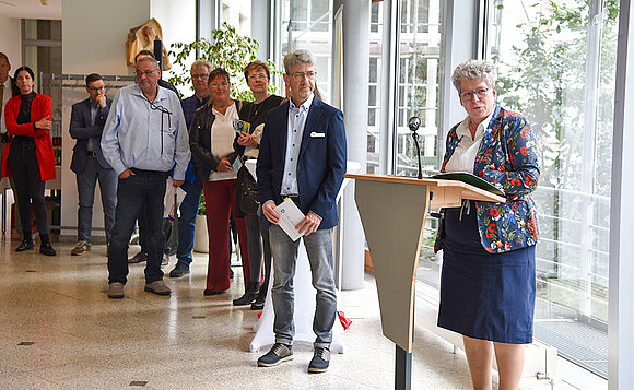 Vizepräsidentin steht am Pult und spricht zu Menschen im Halbrund.